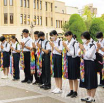 広島の平和記念公園で各自千羽鶴を持って祈る中学生（写真）