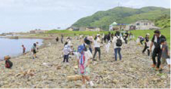 ごみ袋を片手に海岸をきれいにする参加者たち（写真）