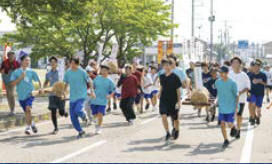 4人1組で米俵を載せたみこしを持ち上げ、走る様子（写真）